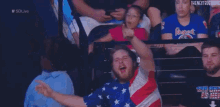 a man in an american flag shirt is sitting in a stadium with other people .