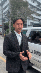 a man in a suit is standing in front of a white la trindad car