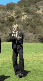 a man in a suit is standing in a grassy field .