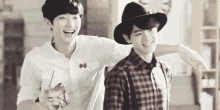 two young men are standing next to each other and laughing . one of the men is wearing a hat .