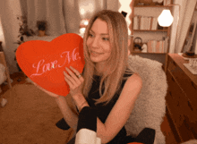 a woman is holding a heart shaped pillow that says " love me "