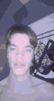 a man without a shirt is making a funny face while standing in front of a bed .
