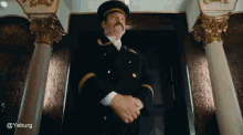 a man in a military uniform with a mustache is standing in front of columns and a door