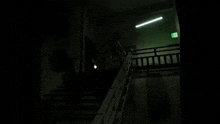 a person is walking down a set of stairs in a dark room with a green exit sign .