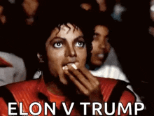 a man in a red jacket is eating popcorn in front of a crowd while watching a movie .