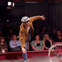 a man wearing a helmet stands in front of a crowd and a bicycle