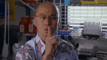 a bald man wearing glasses is holding his finger to his lips .