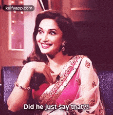 a woman in a pink saree is sitting on a chair and smiling .