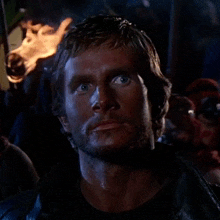 a close up of a man 's face with a fire torch in the background