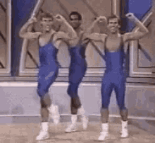 three men in blue leotards are dancing together on a stage .
