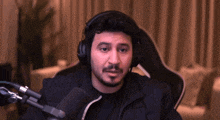a man wearing headphones is sitting in front of a microphone in a chair .