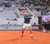 a tennis player is swinging a racket in front of an emirates banner