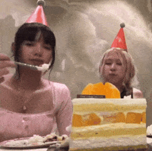two girls wearing party hats are eating a piece of cake