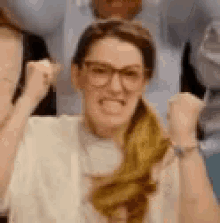 a woman wearing glasses is making a funny face while raising her fist in the air .