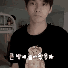 a young man wearing a black t-shirt with a teddy bear on it is standing in a room .