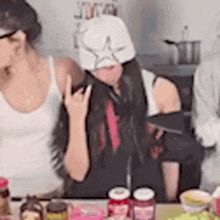 two women are sitting at a table with jars of food .