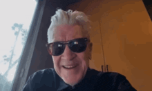 an older man wearing sunglasses and a black shirt is smiling