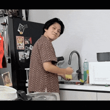 a man in a striped shirt is washing dishes in a kitchen with a microwave in the background