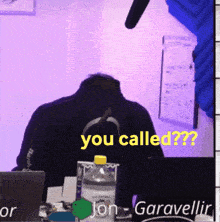 a man sitting at a desk with a laptop and a bottle of water with the words you called on it