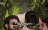 a man with a beard is talking to another man while wearing a pair of glasses .