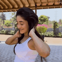 a woman in a white tank top holds her hair