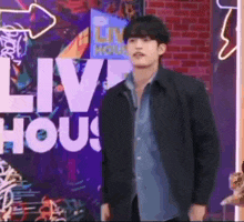 a man in a black jacket is standing in front of a neon sign that says live house .