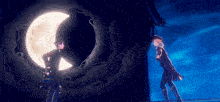 a couple of people standing in front of a full moon