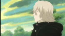 a man with blonde hair and a black jacket is standing in a field with trees in the background .