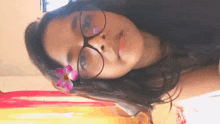a girl wearing glasses and a flower in her hair is looking at the camera .