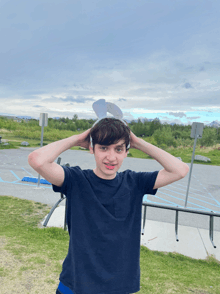 a boy wearing a blue shirt holds his hands to his head in front of a parking lot