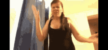 a woman in a black tank top is standing in front of a blue curtain .