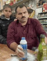 a man in a maroon shirt is holding a bottle of water that says bridge