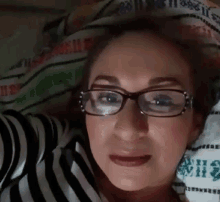 a woman wearing glasses and a striped shirt is laying on a bed