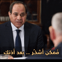 a man in a suit and tie is talking to another man with arabic writing behind him