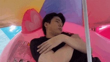 a man is laying on a pink inflatable unicorn under an umbrella .