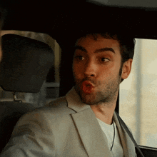 a man in a suit making a funny face while sitting in a car