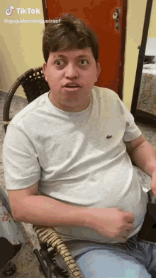a man in a white shirt with a lacoste logo on it is sitting in a chair ..