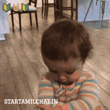 a baby in a striped shirt is looking down with the words starttamilchat.in below it
