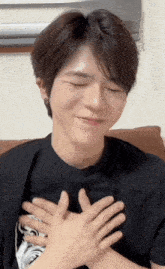 a young man is sitting on a couch with his hands on his chest .