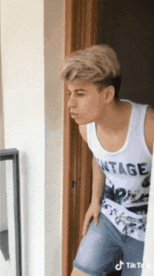 a young man wearing a tank top that says vintage is standing in front of a door .