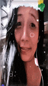 a woman wearing a santa hat and earbuds looks at the camera