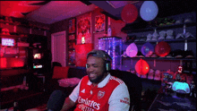 a man wearing a red emirates jersey sits in a room
