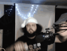a man with a beard is wearing a santa hat and holding a microphone in front of him