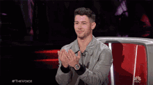 a man applauds while sitting in front of a nbc sign