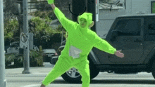 a person in a neon green teletubbies costume is dancing on the street .