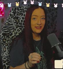 a woman giving a thumbs up in front of a microphone with the letter x in the corner
