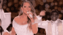 a woman in a white dress is singing into a microphone in front of a crowd .