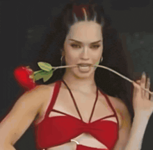 a woman in a red top has a rose in her mouth
