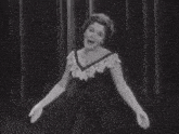a woman in a black dress is standing in front of a curtain