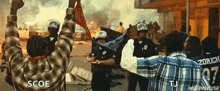 a man in a plaid shirt is holding a bandana in front of riot police .